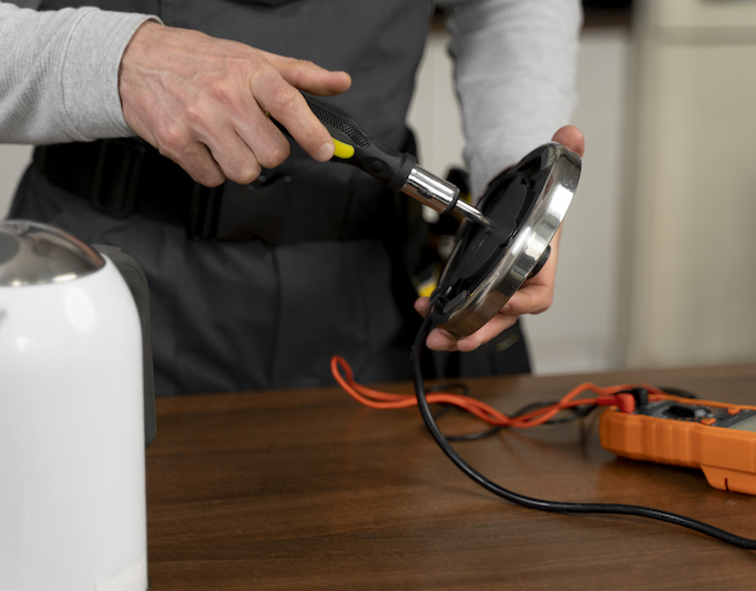 A male electrician providing expert Farnham electrical services by repairing kitchen appliance with screwdriver and multi-meter.